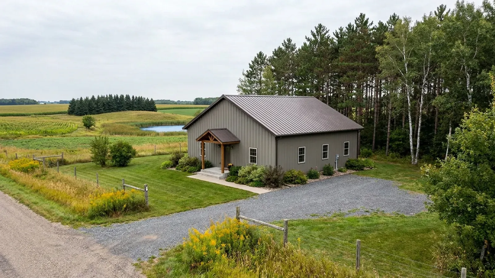A compact 30x40 barndominium sized like a starter home or cabin, with a covered entry porch, no large shop bay, and pines and birches at the edge of the yard.